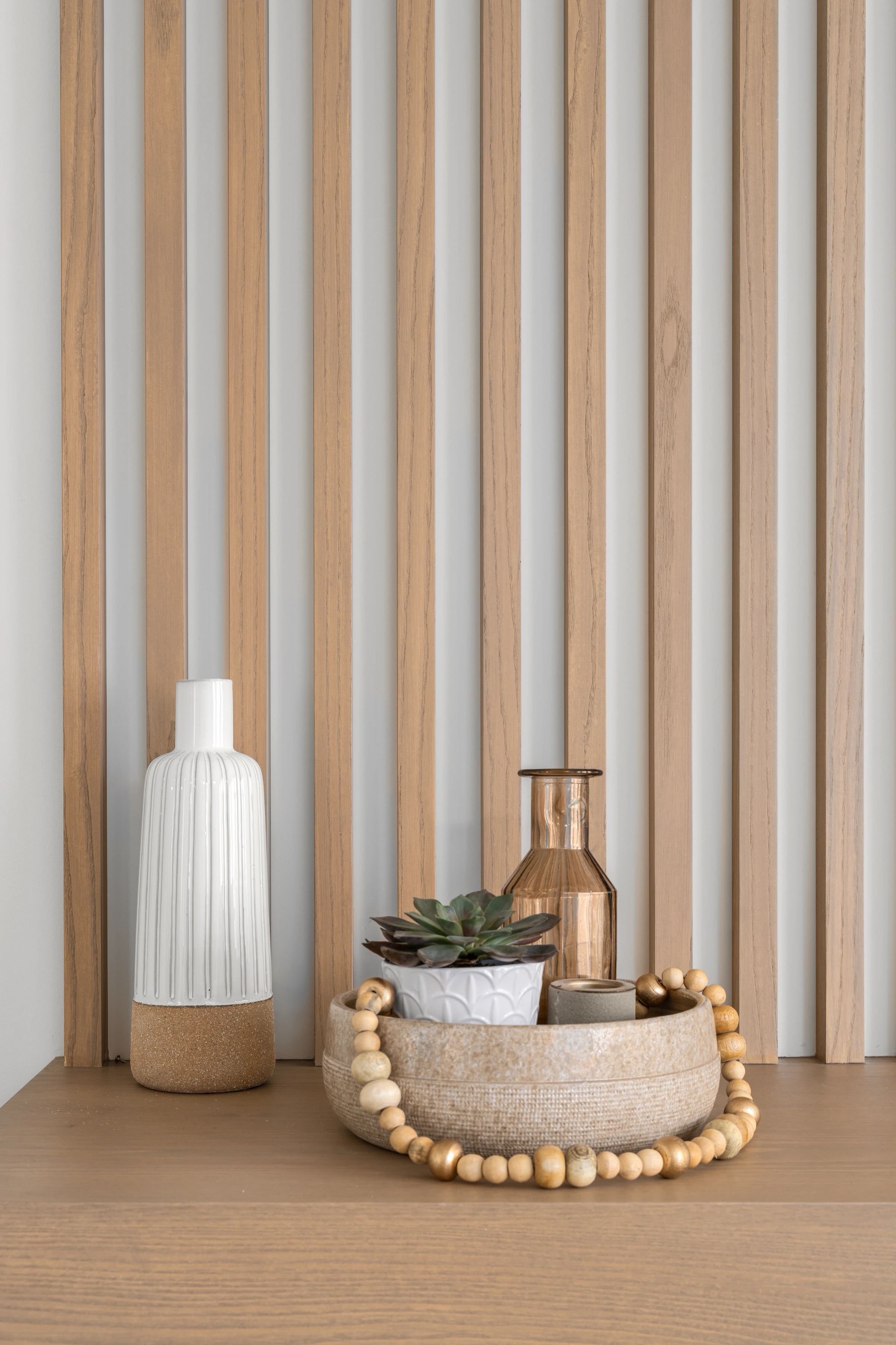 Styled vignette of a ceramic vase, succulent, and wood beads on a built-in desk