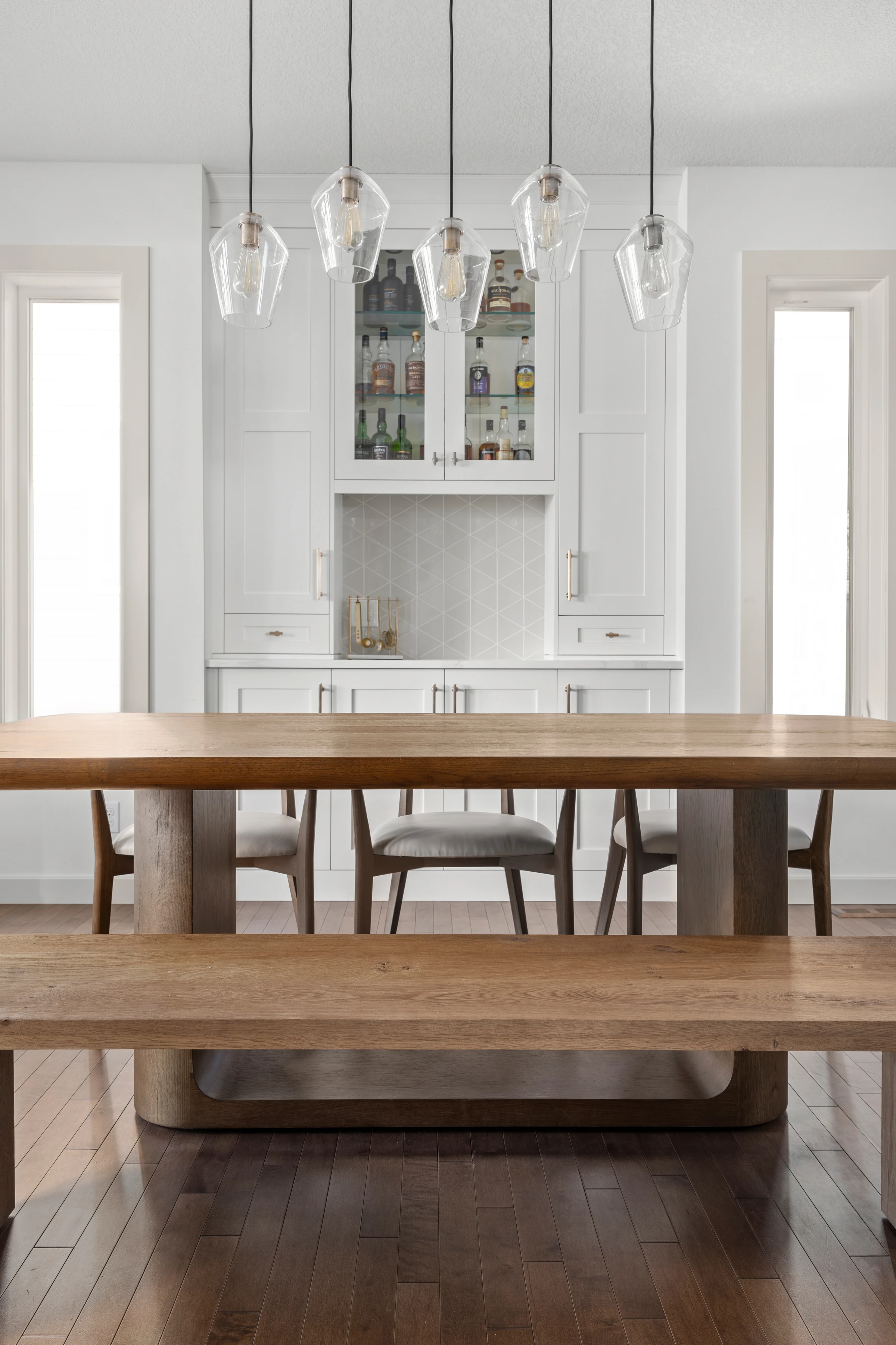 Dining table facing a built-in bar cabinet beneath a row of glass pendant lights