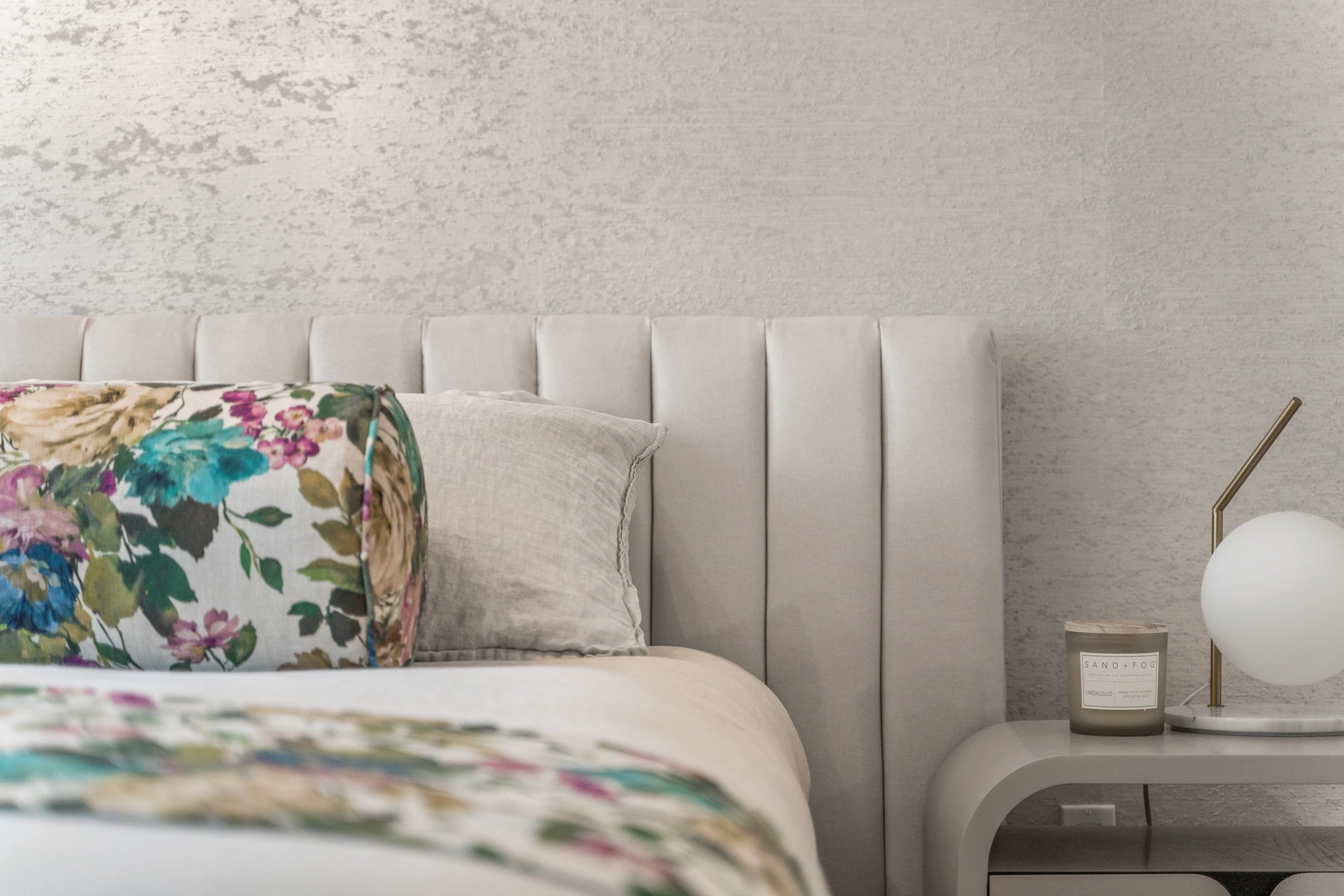 Channel-tufted headboard detail with floral bedding and a round nightstand lamp