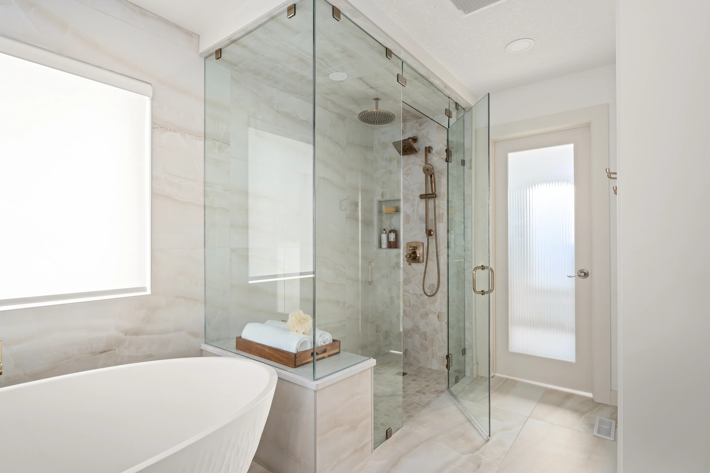 Glass-enclosed shower and freestanding tub in a bright marble ensuite