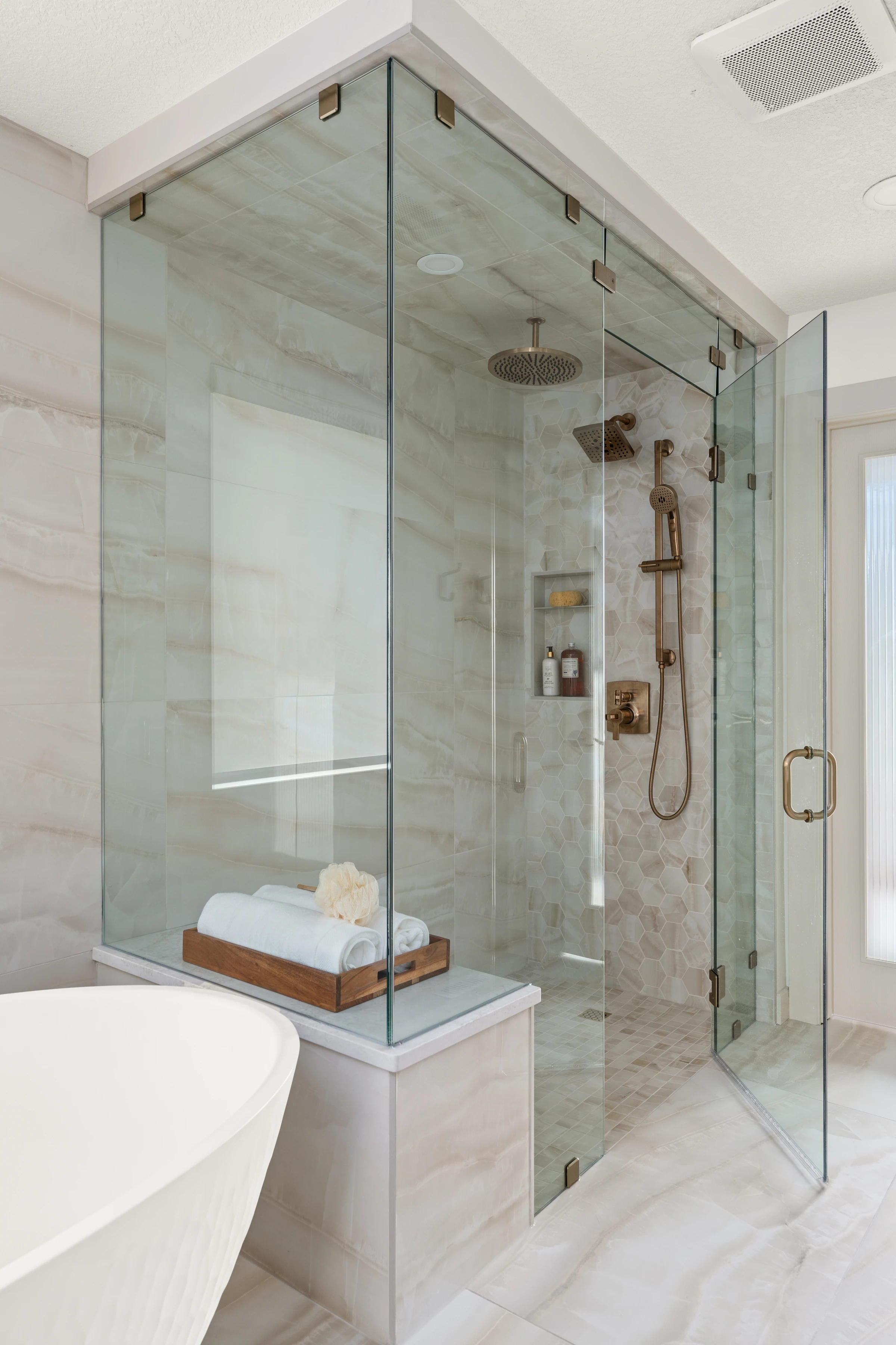 Brass-fitted glass shower with a marble bench and folded towels
