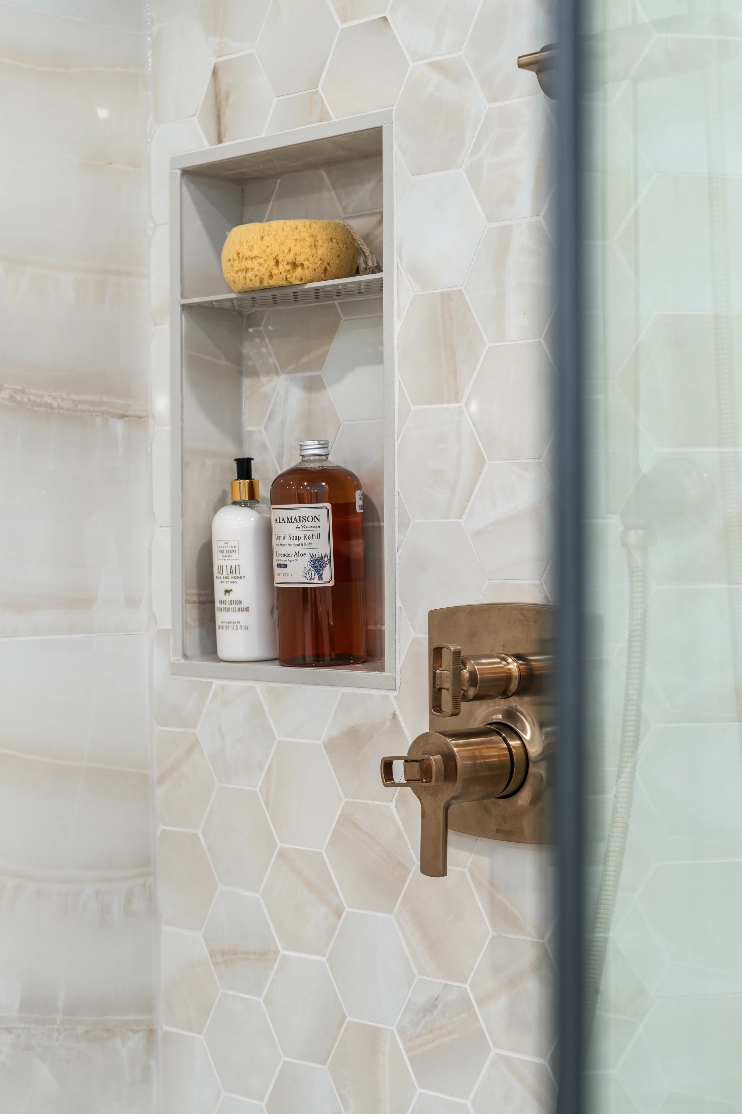 Marble tile shower niche detail with brass fixtures and bath products