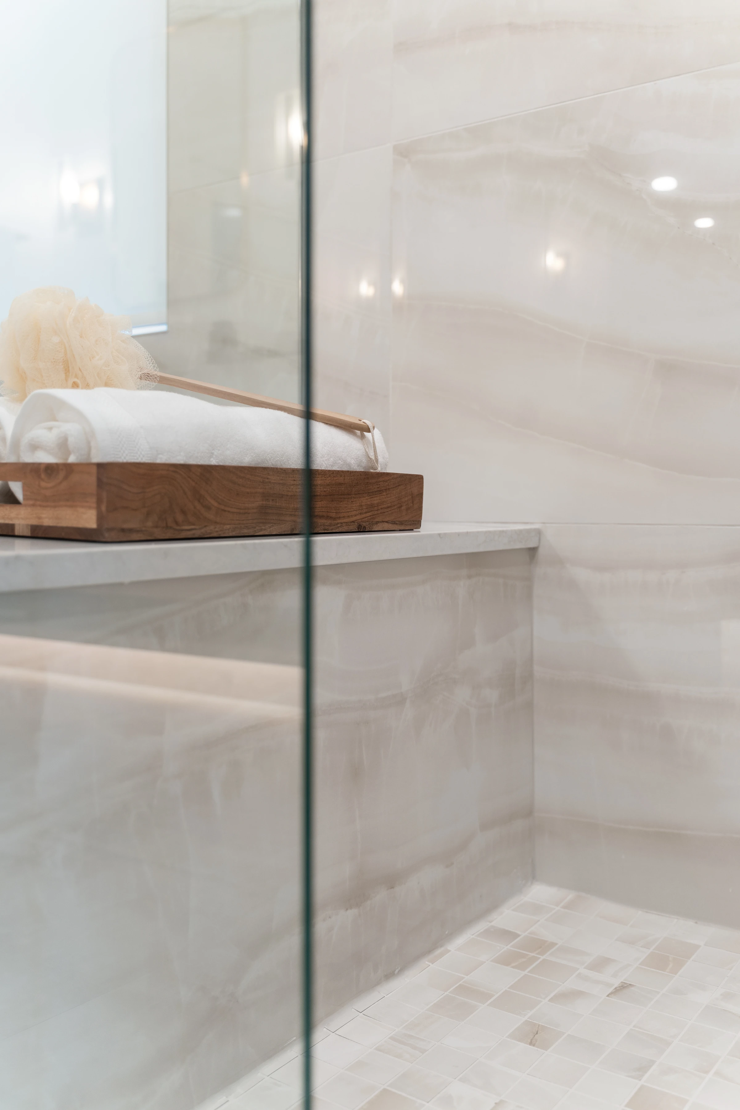 Detail of a glass shower ledge with a wood towel tray in a marble ensuite