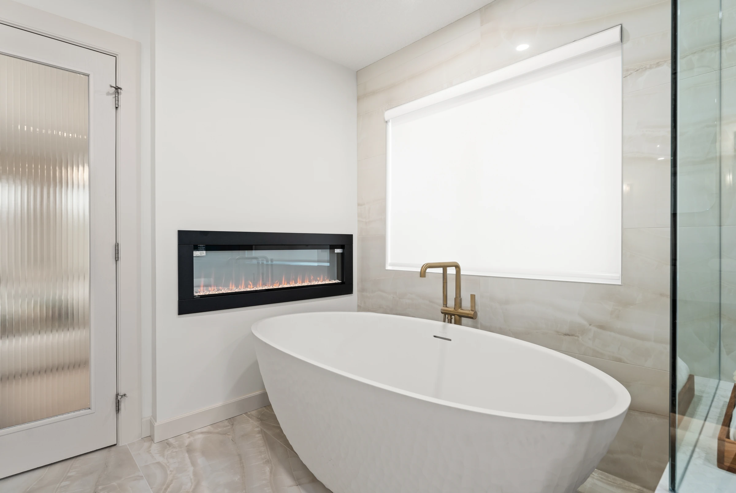 Freestanding tub beneath a linear fireplace and a gold filler in a primary ensuite