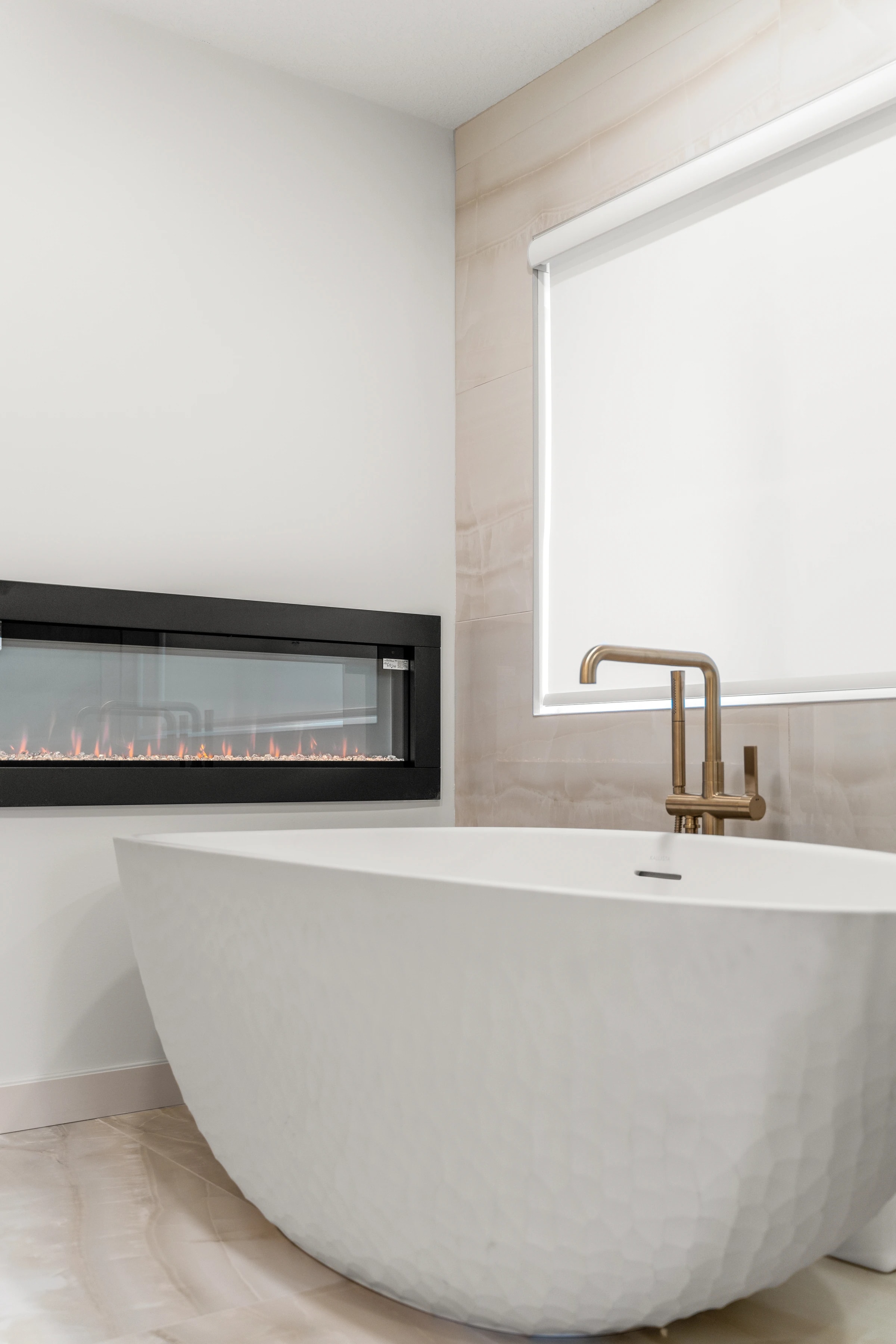 Detail of a brass tub filler beside a built-in linear fireplace