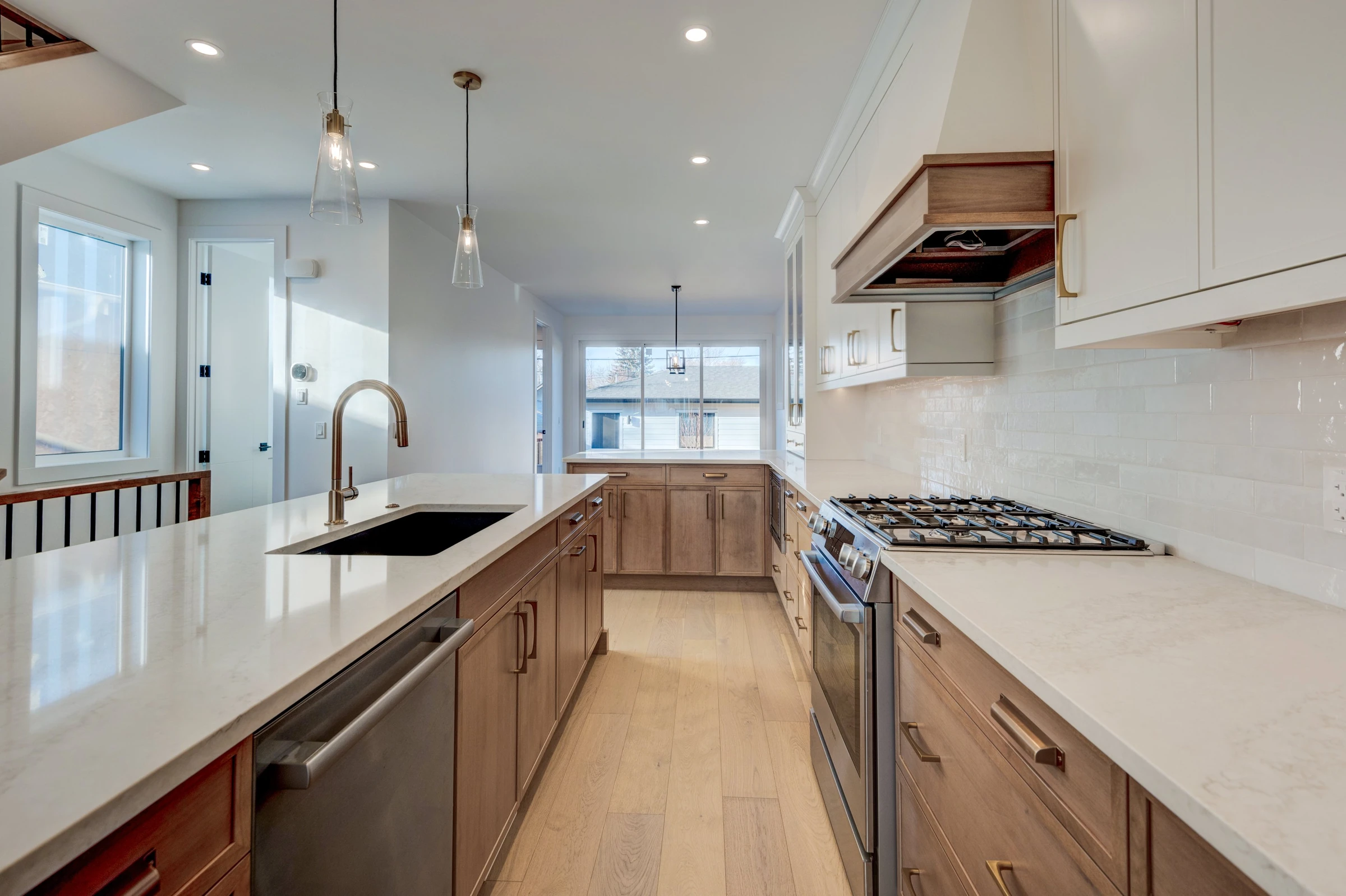 Galley kitchen with two-tone wood cabinetry, subway tile backsplash, and gold hardware