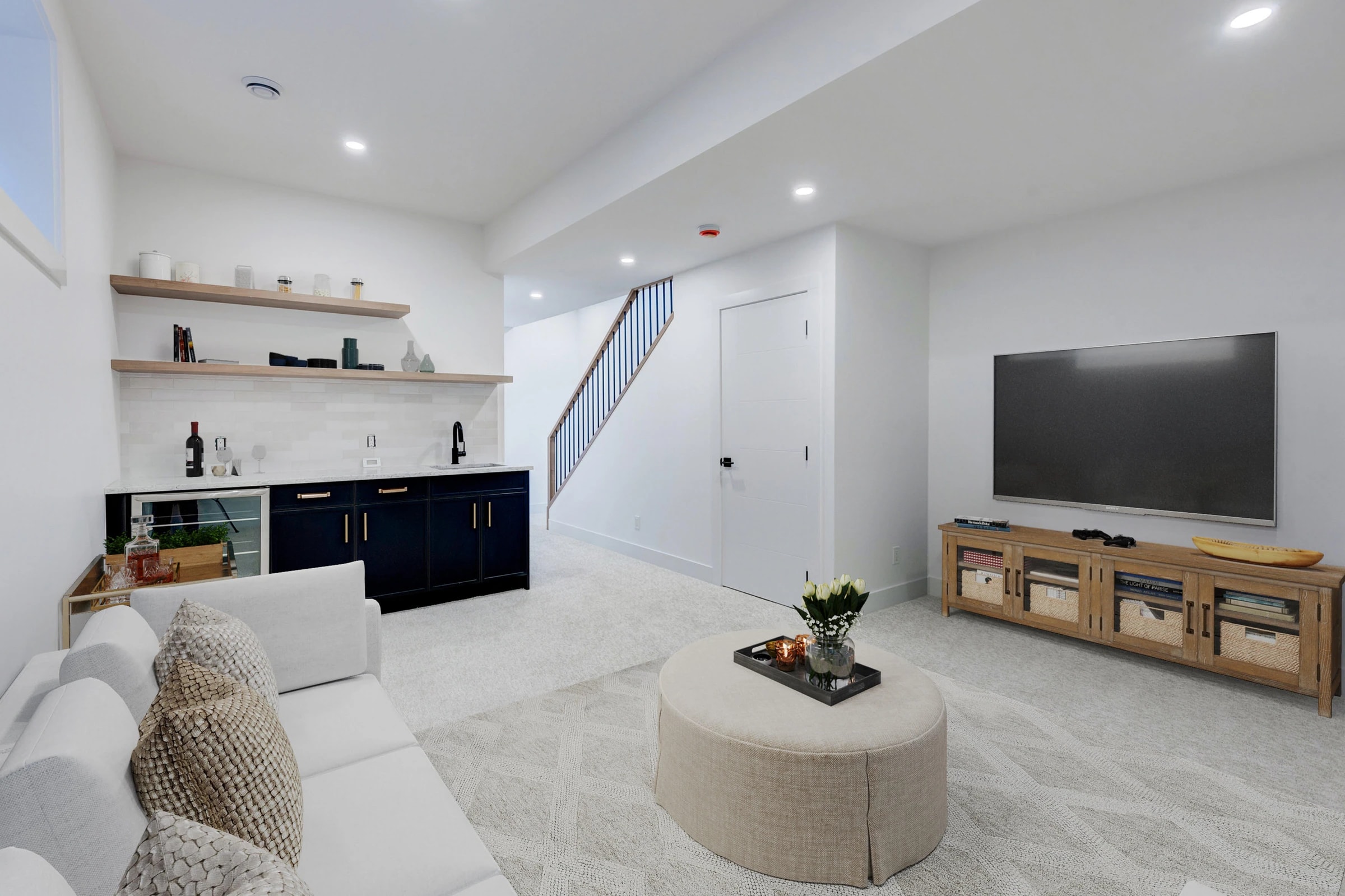 Basement rec room with a built-in navy cabinet, open shelving, and a media wall