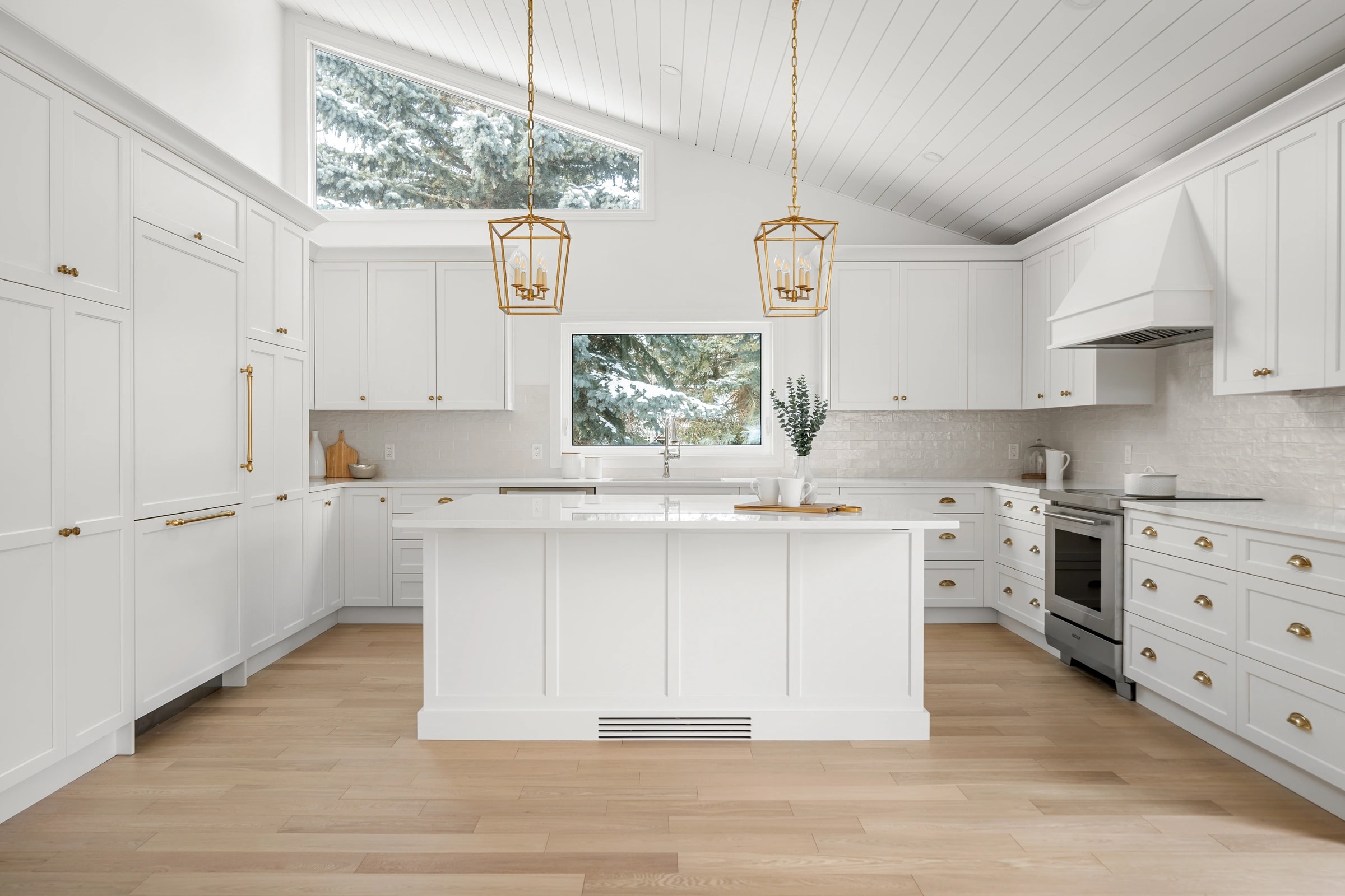 Bright white shaker kitchen with a center island, brass lantern pendants, and a shiplap vaulted ceiling