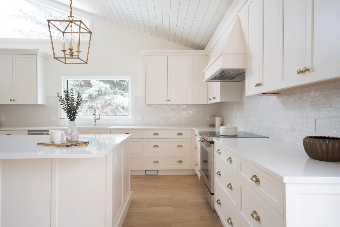 Corner of a white shaker kitchen with a brass lantern pendant, a styled island, and a window onto snowy spruce trees