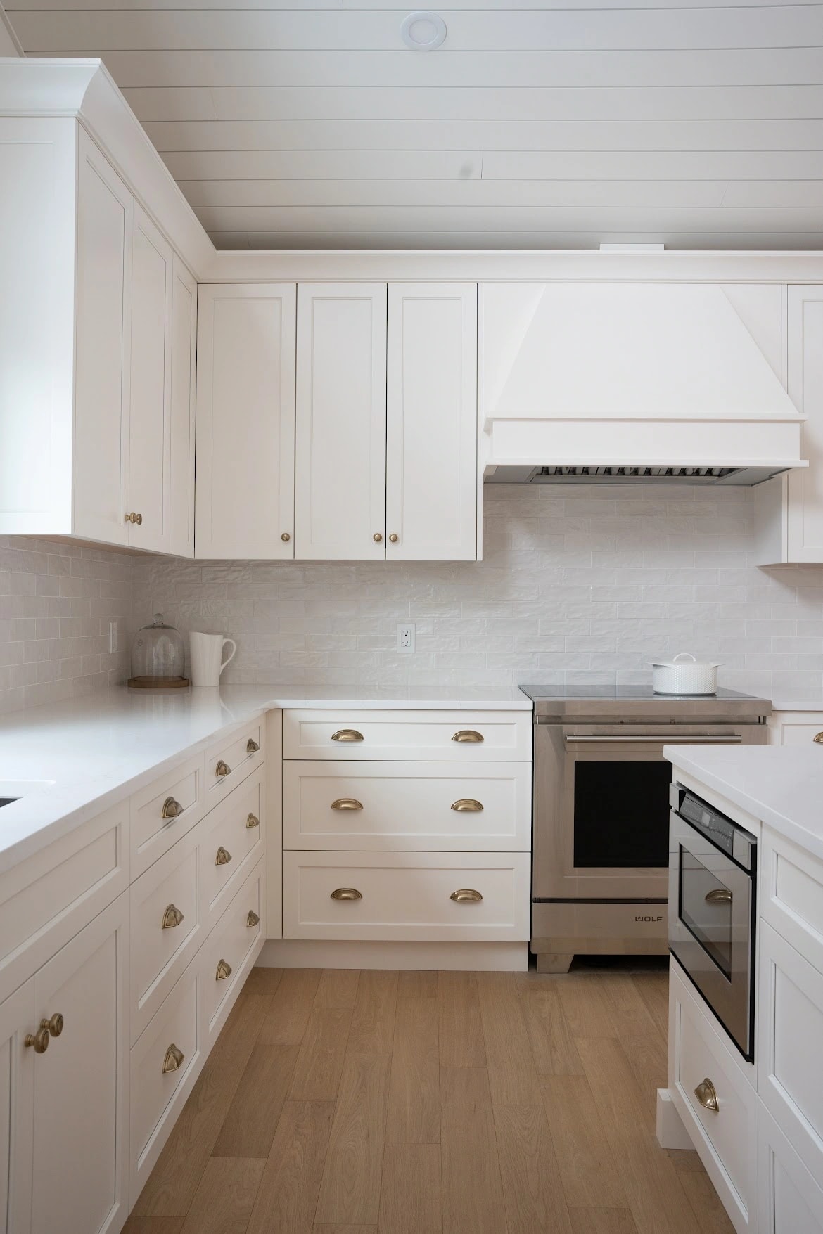 White shaker cabinetry with brass cup pulls, a stainless range, and a hand-glazed tile backsplash