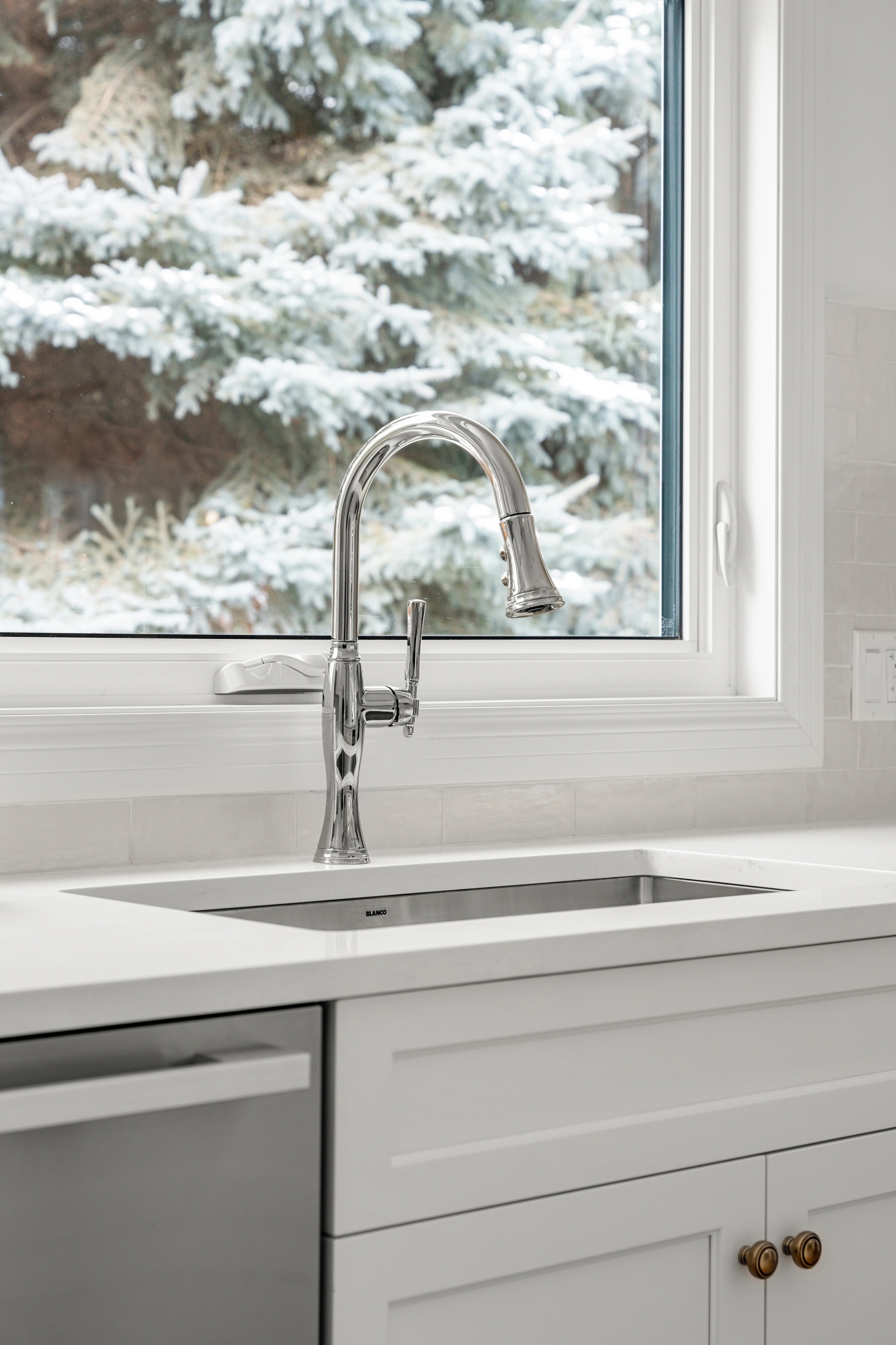 Polished chrome pull-down faucet over an undermount sink, framed by a window onto snow-covered trees