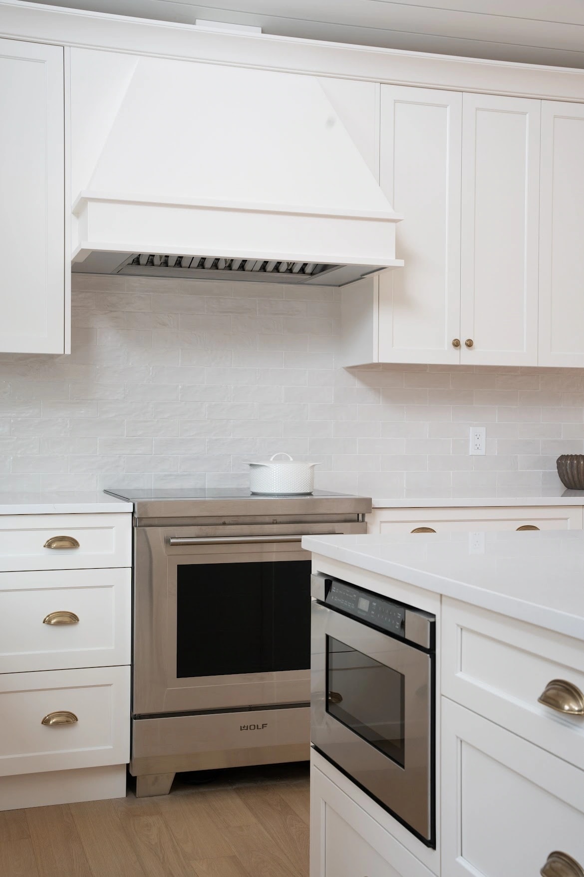 Painted range hood above a professional range with a textured white tile backsplash and a drawer microwave