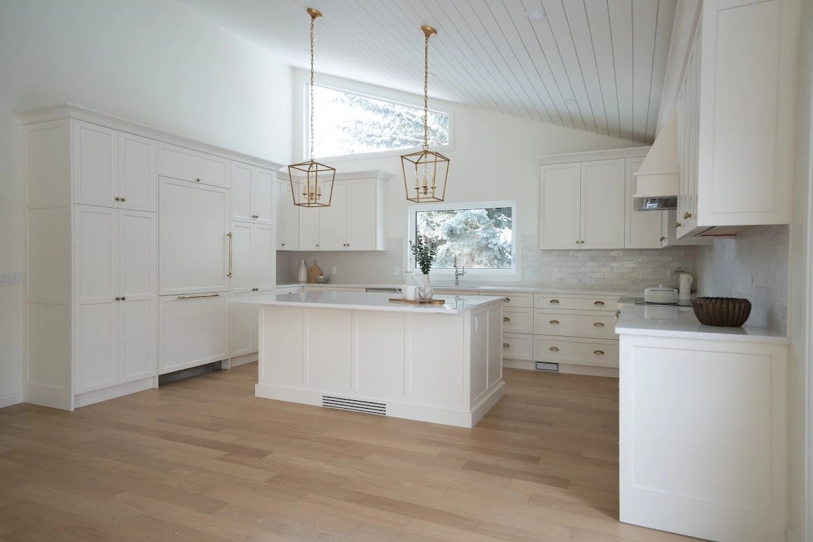 Wide view of a white shaker kitchen with brass lantern pendants, an island, and a vaulted shiplap ceiling