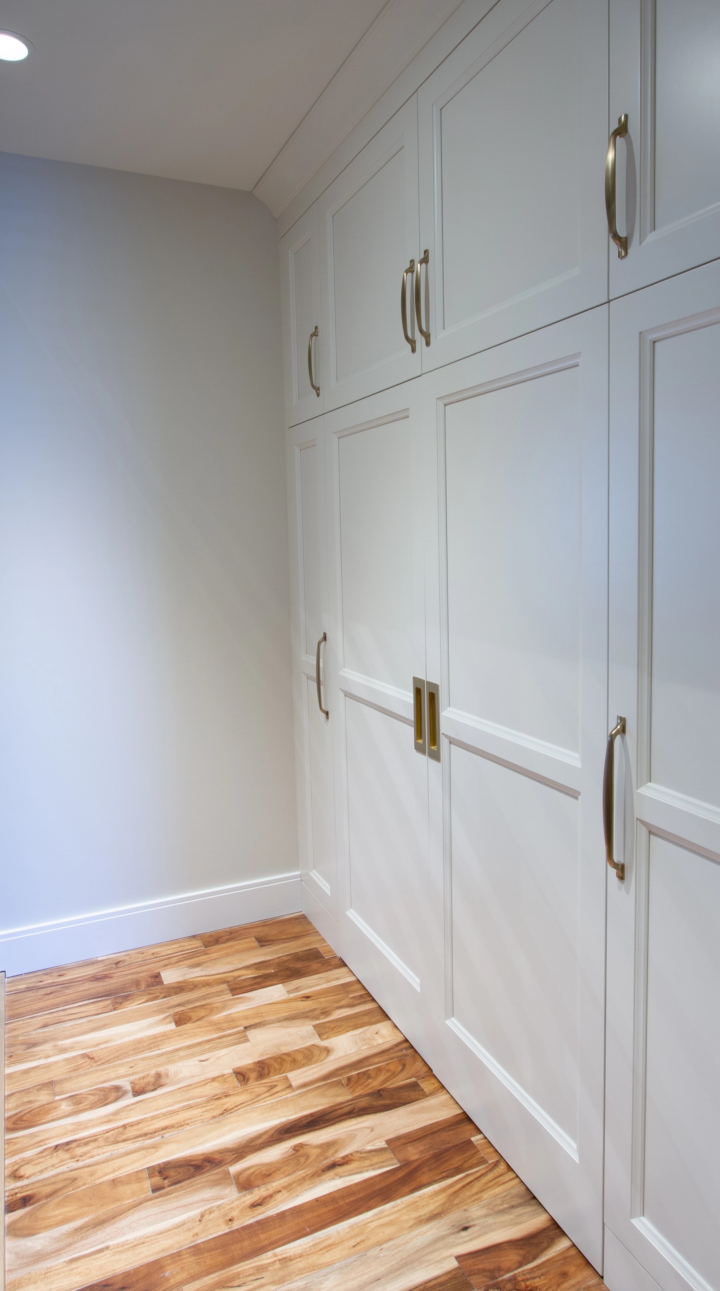 Walk-in closet with white shaker cabinetry and brass hardware