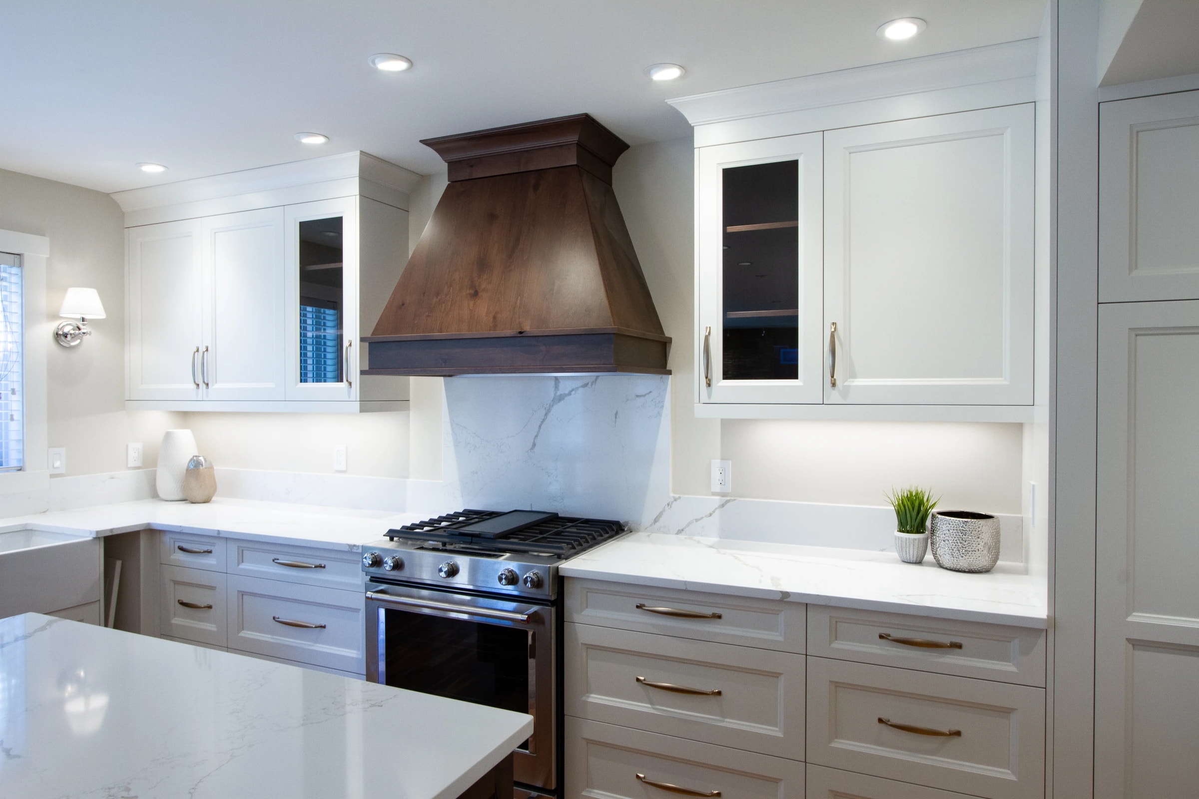 Kitchen with a wood range hood, white cabinetry, and brass hardware