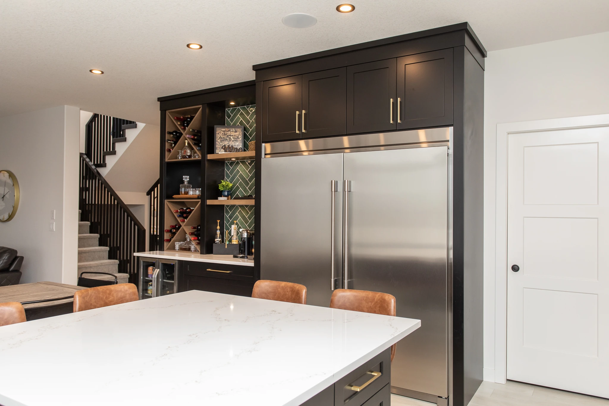 Kitchen island view of a dark navy butler's pantry with wine storage and a staircase beyond