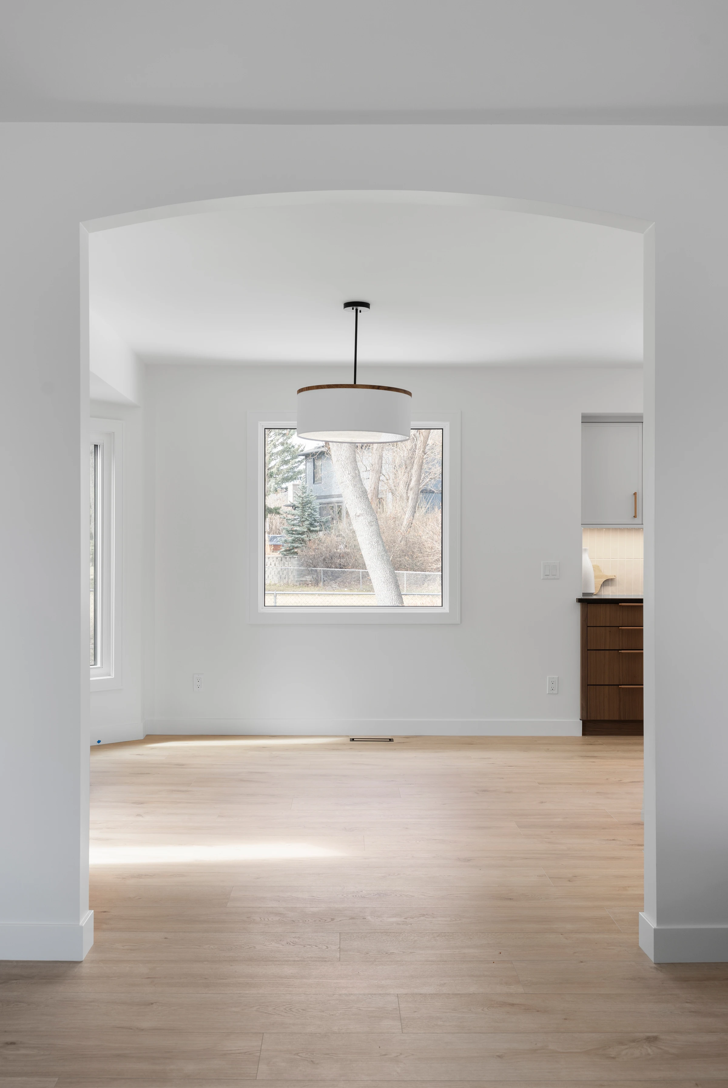 Arched doorway framing a sunlit dining nook with a drum pendant light