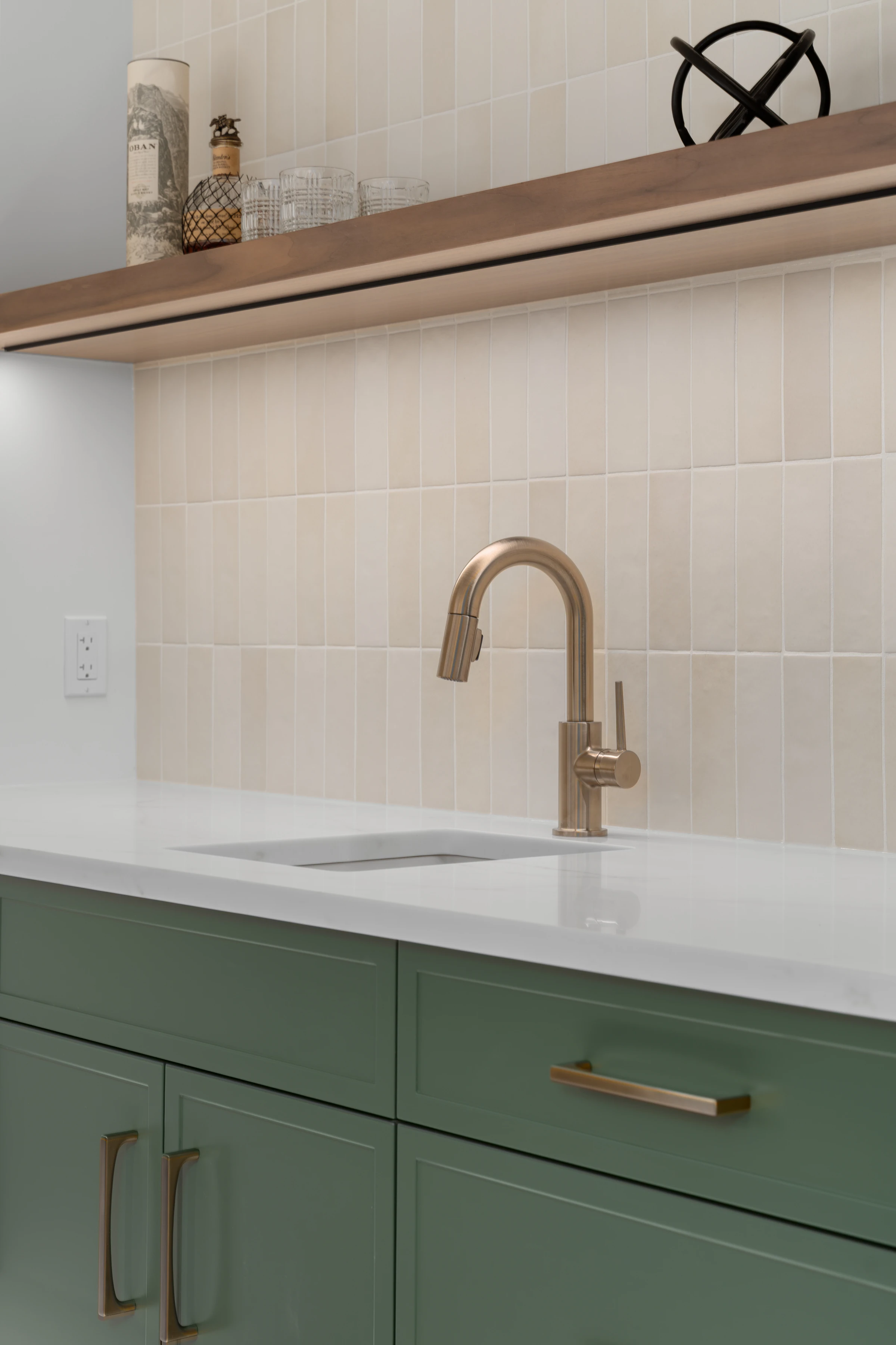Brass faucet and tile backsplash detail above green cabinetry