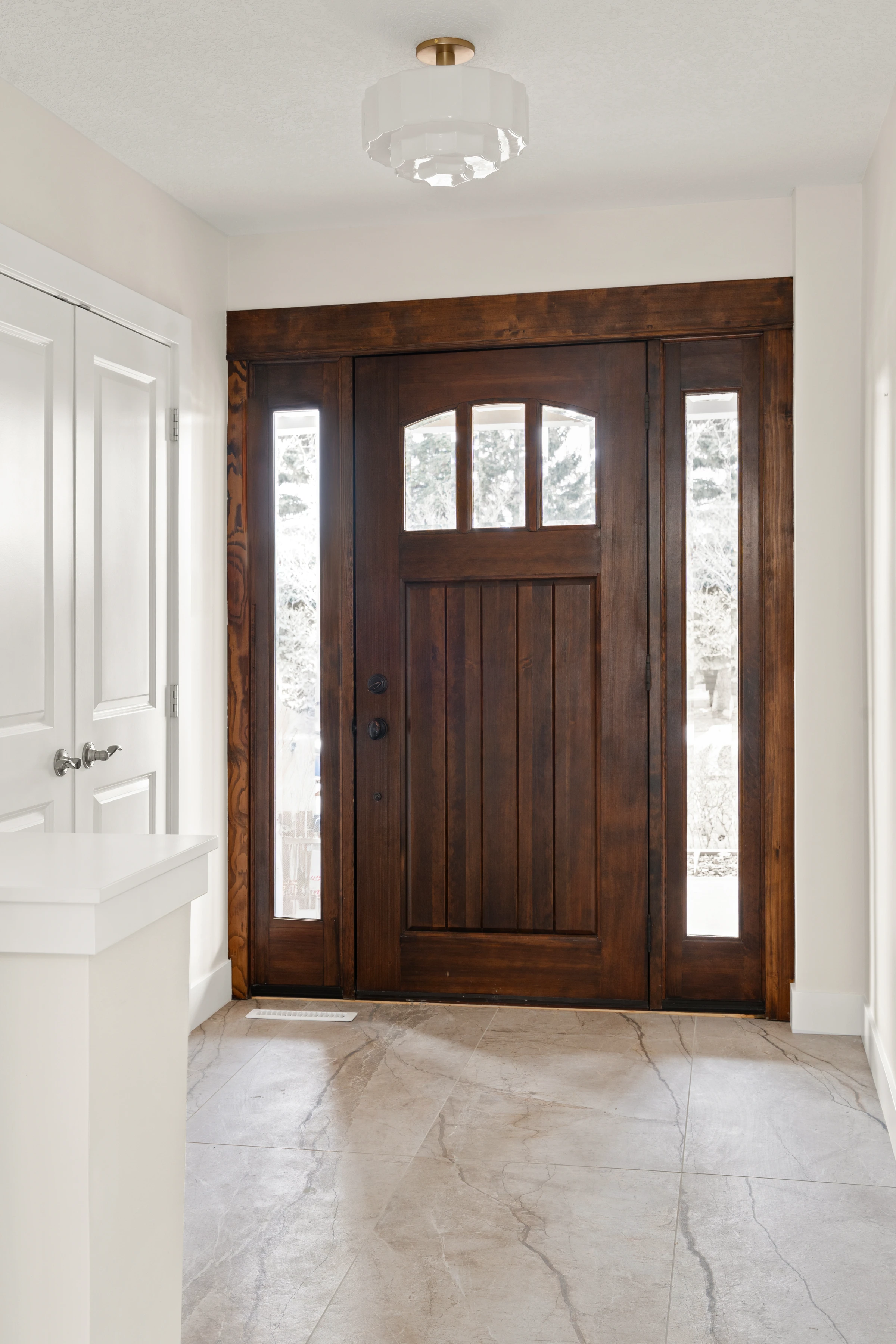 Entryway with a solid wood front door, glass sidelights, and marble-look tile flooring