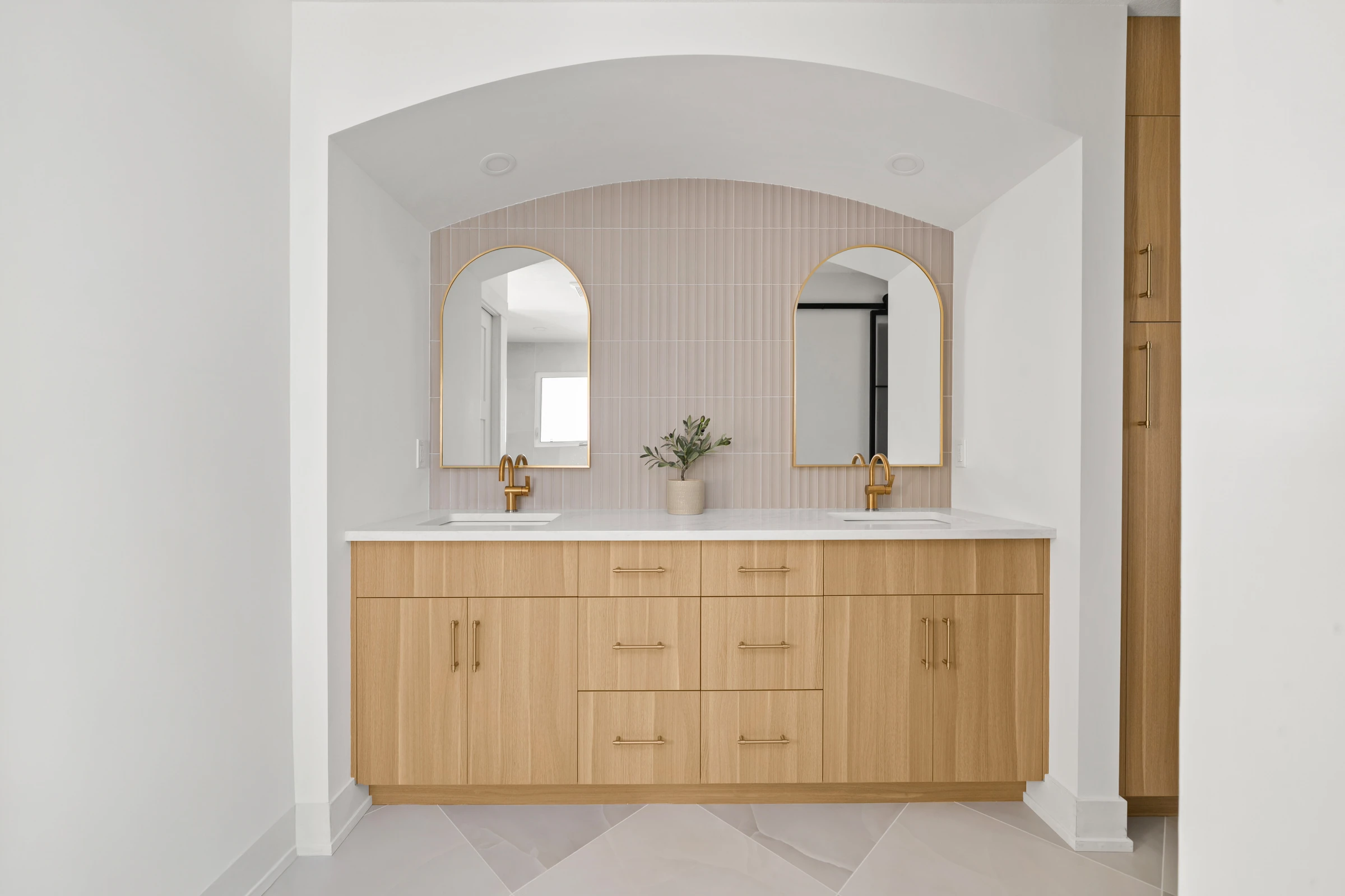 Primary ensuite with an arched alcove, double vanity, and pink tile behind gold-framed mirrors