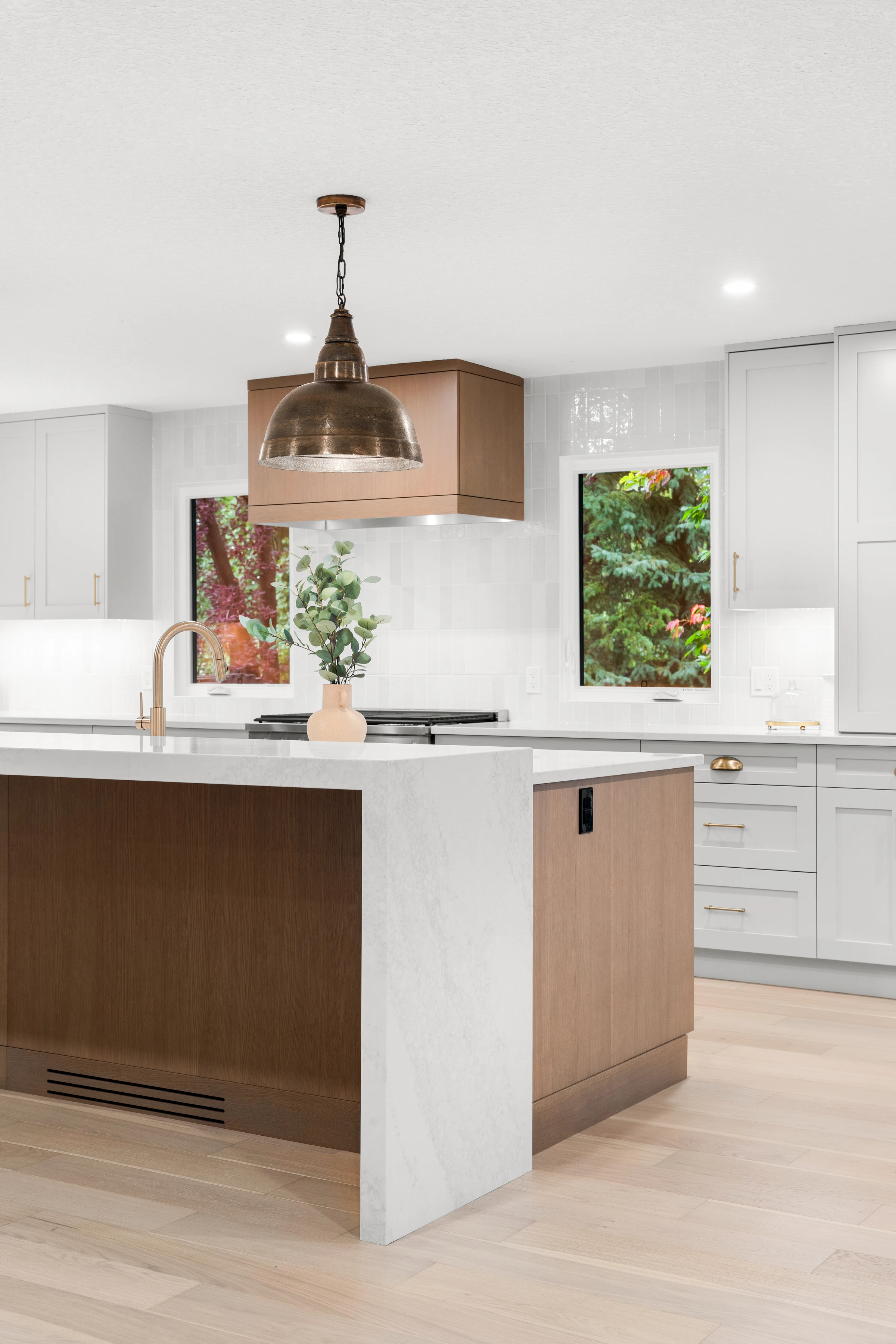 Kitchen island with copper pendant lighting and framed botanical art flanking the range