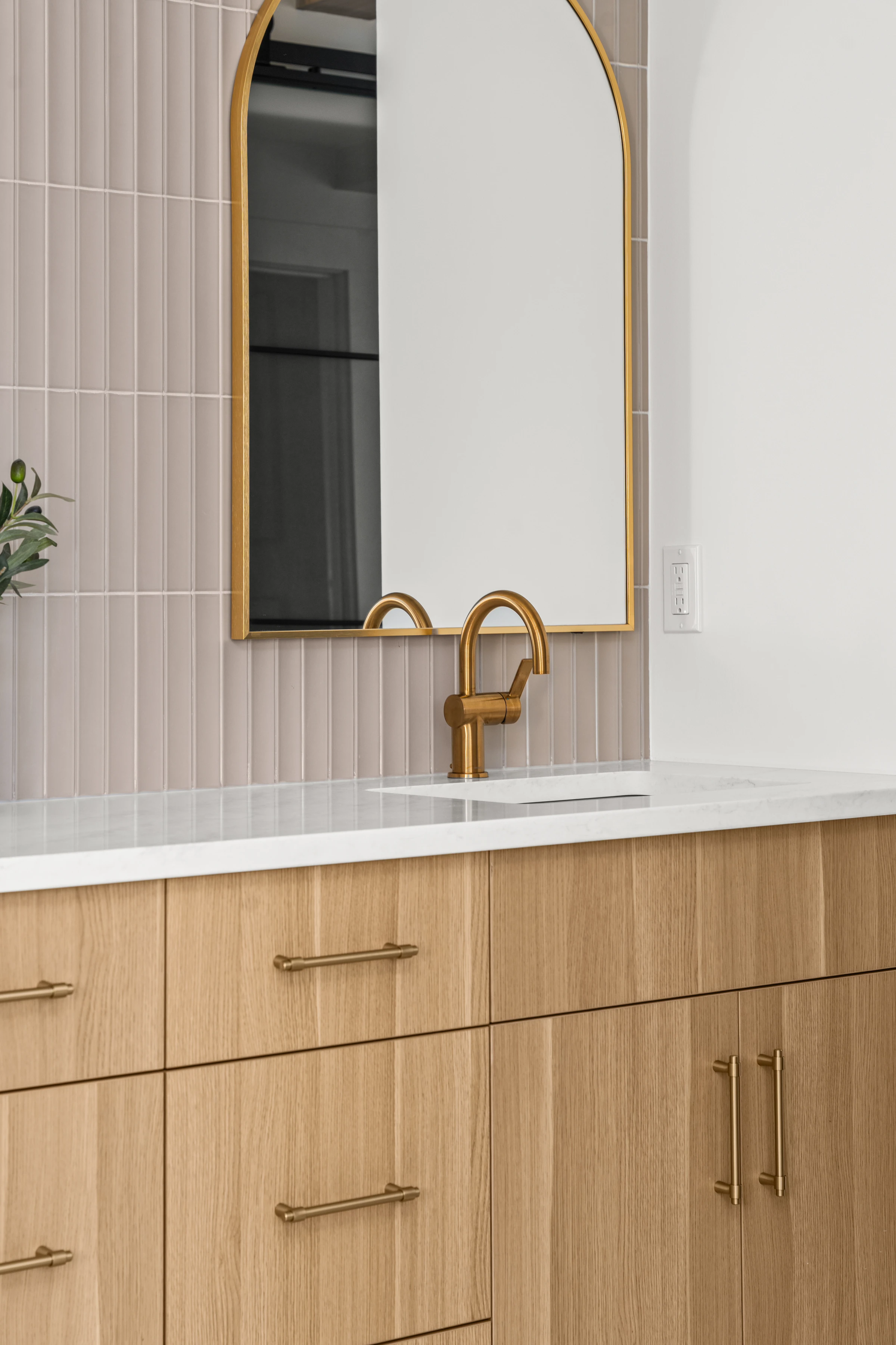 Detail of a gold-framed arched mirror and matching faucet above a white oak vanity