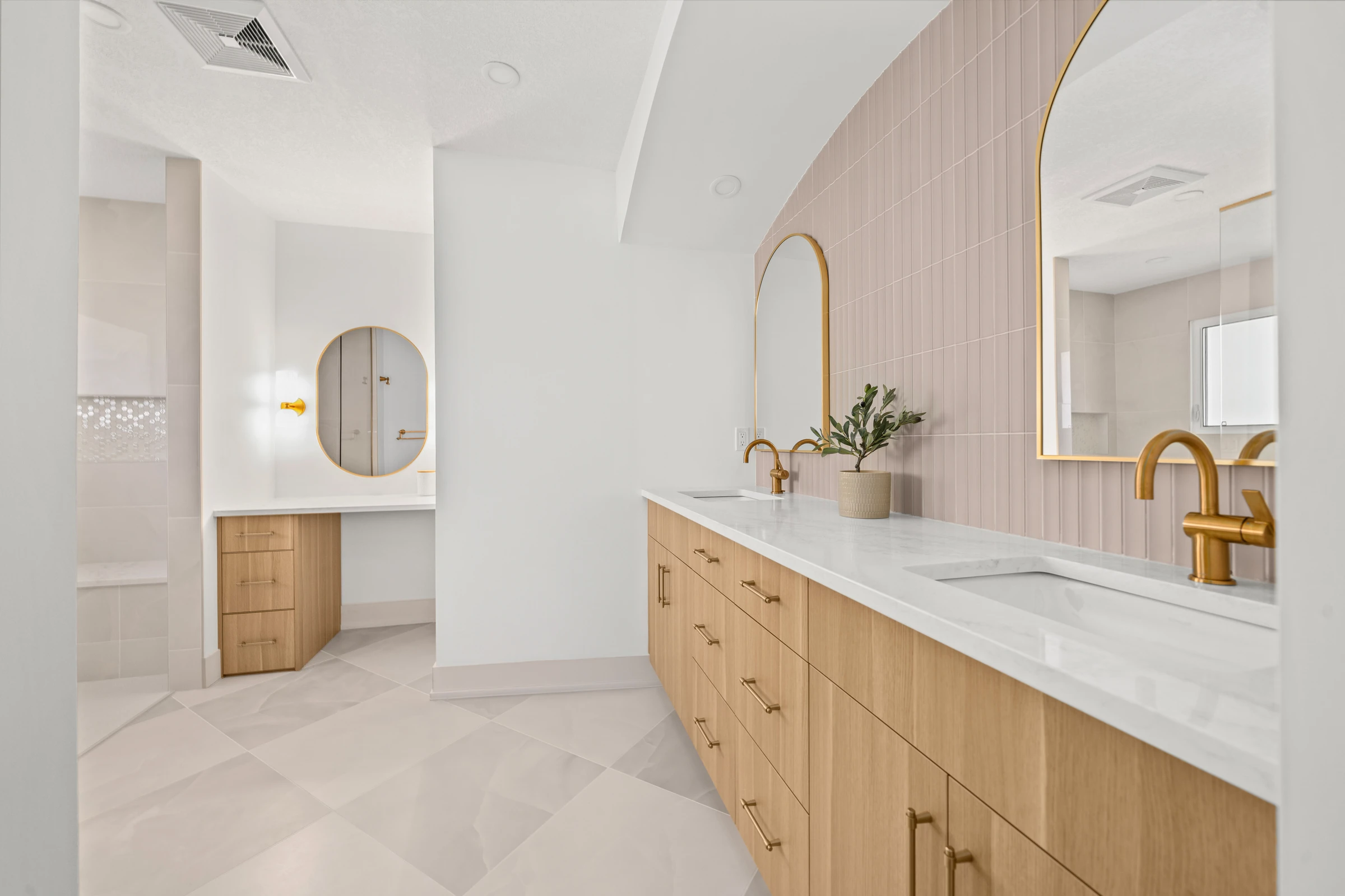 Curved pink accent wall behind a double vanity with gold fixtures and an arched mirror