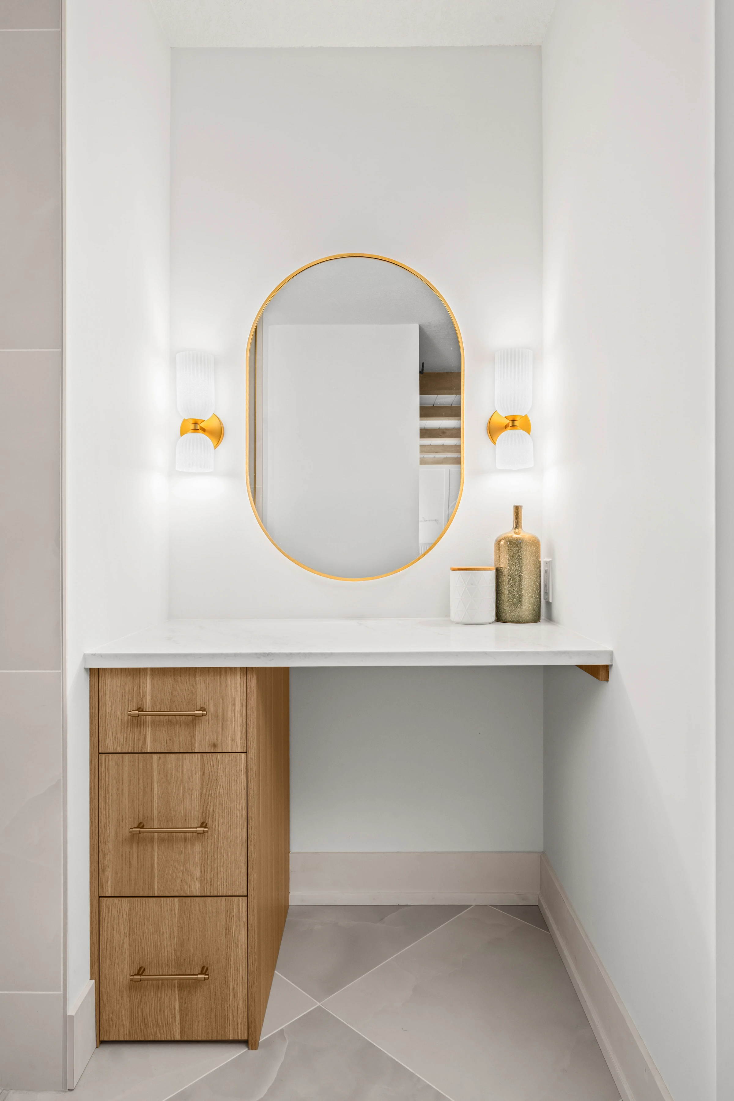 Powder nook with an oval gold mirror, sconces, and built-in wood drawers
