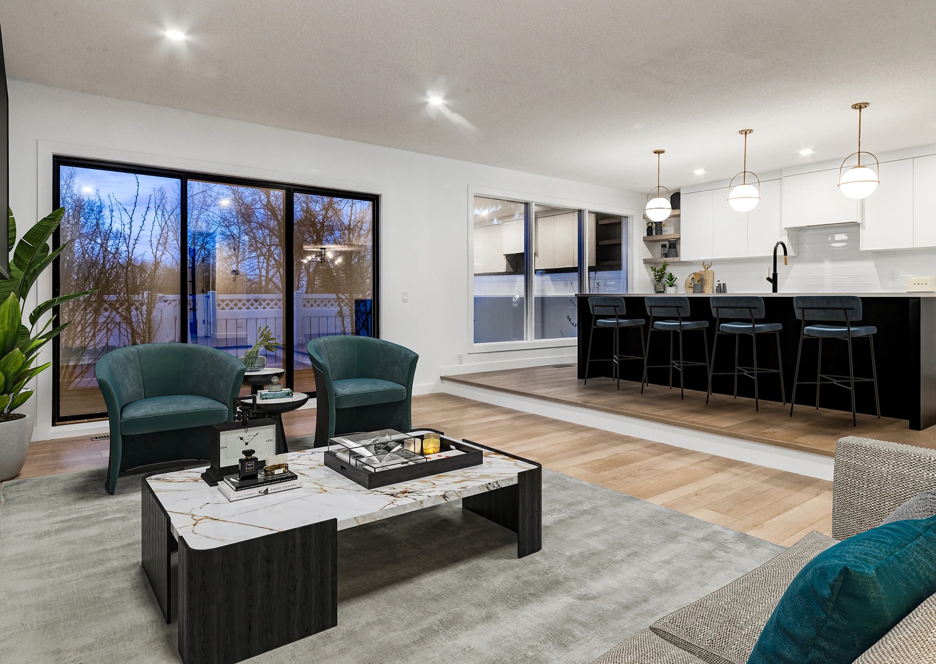 Virtually staged open-concept living area with teal accent chairs and a black kitchen island beyond