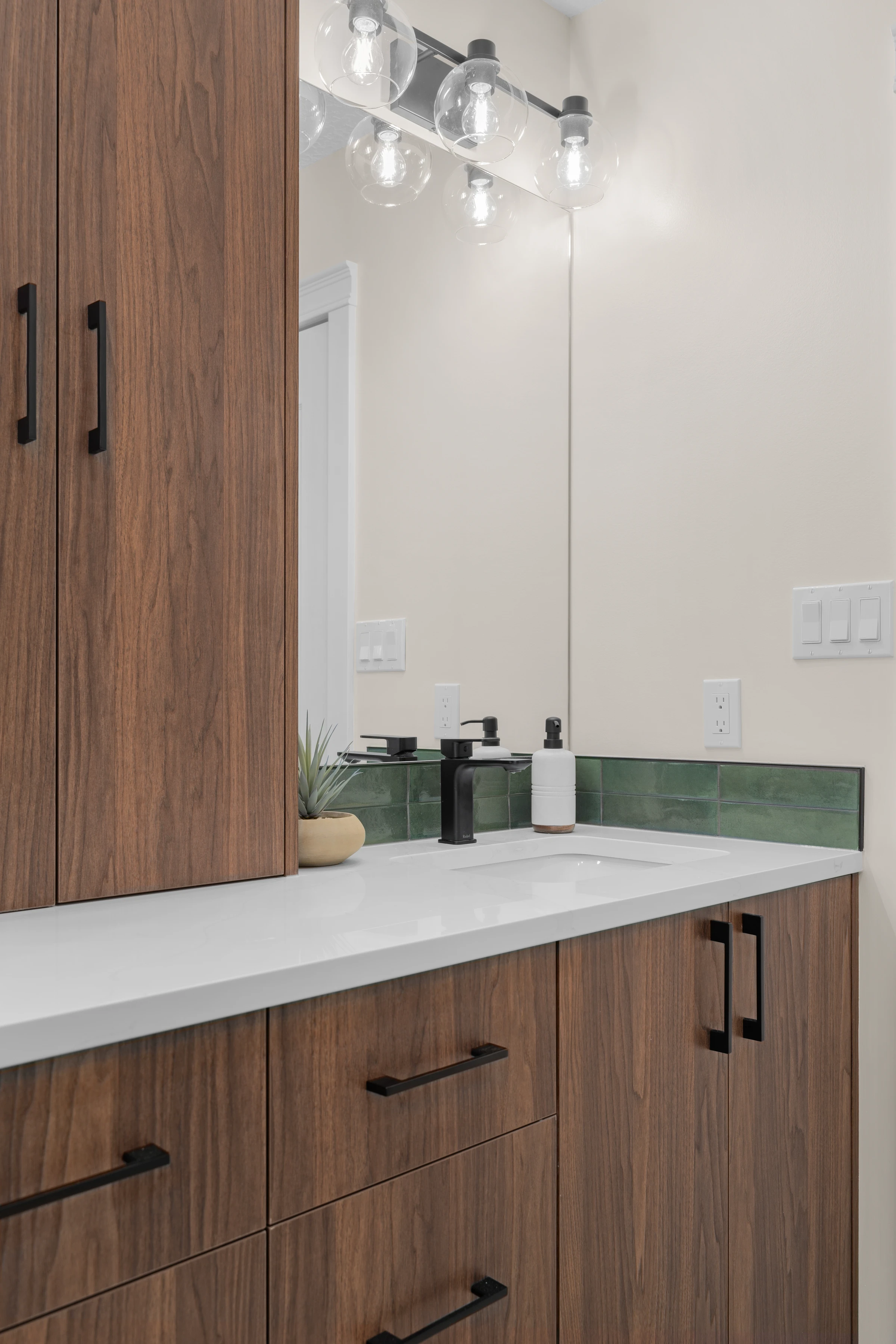 Detail of walnut vanity cabinetry with green tile and black hardware