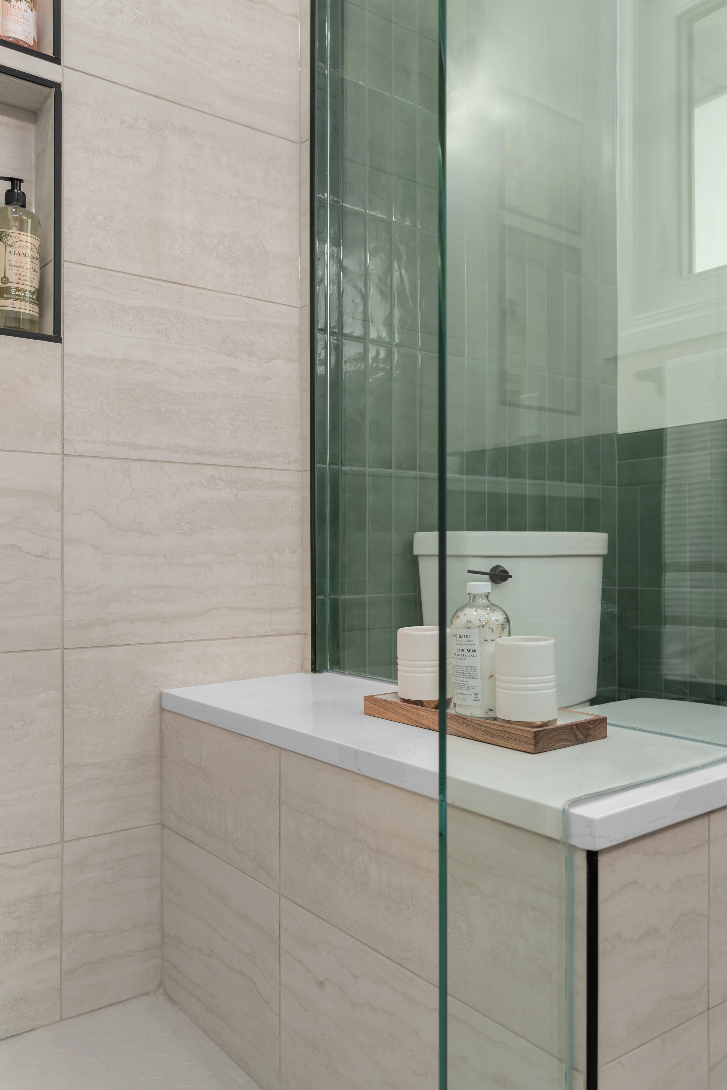 Glass shower detail with a green tile accent and a marble bench