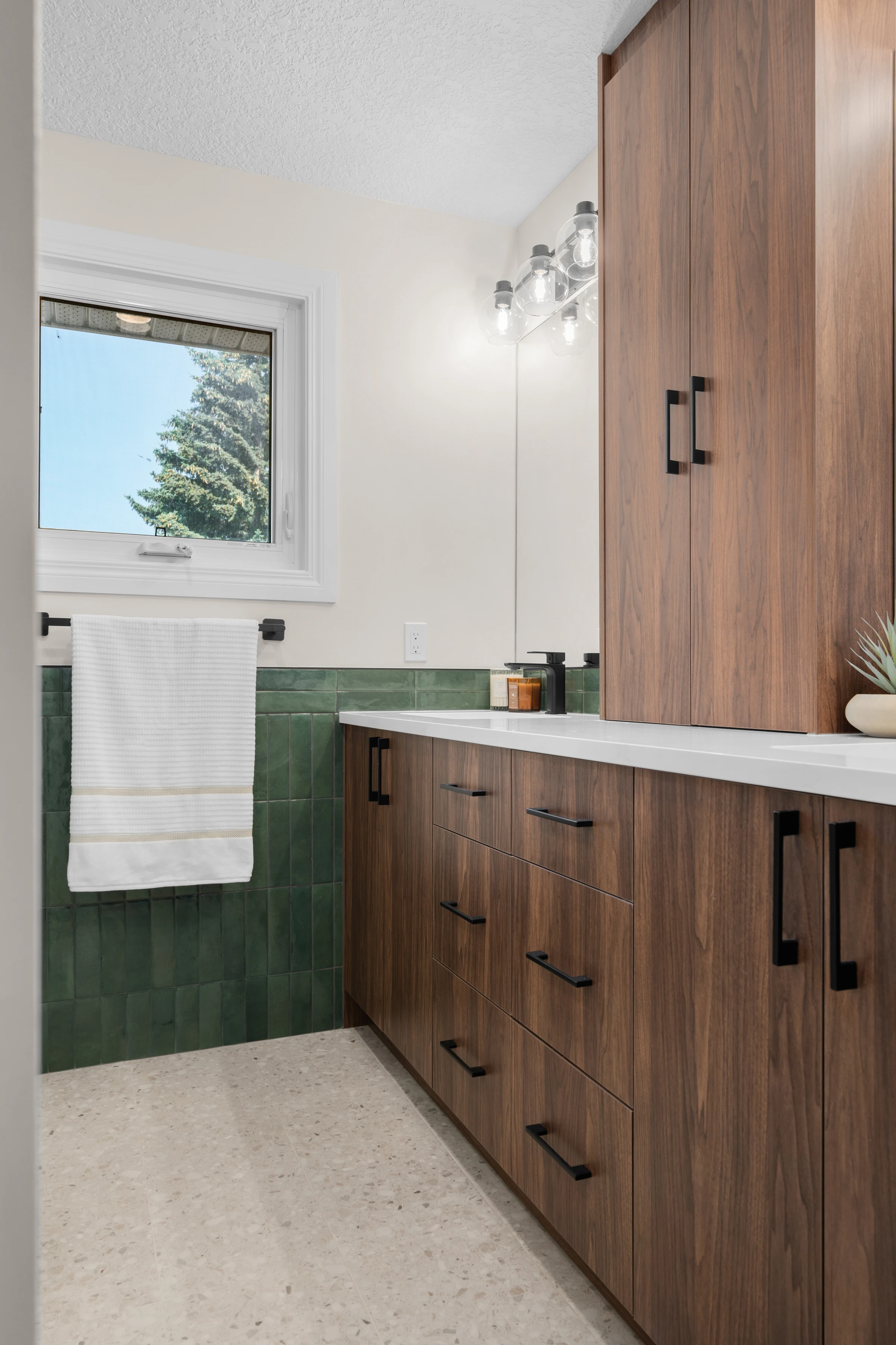 Walnut vanity wall with green tile backsplash beneath a bright window