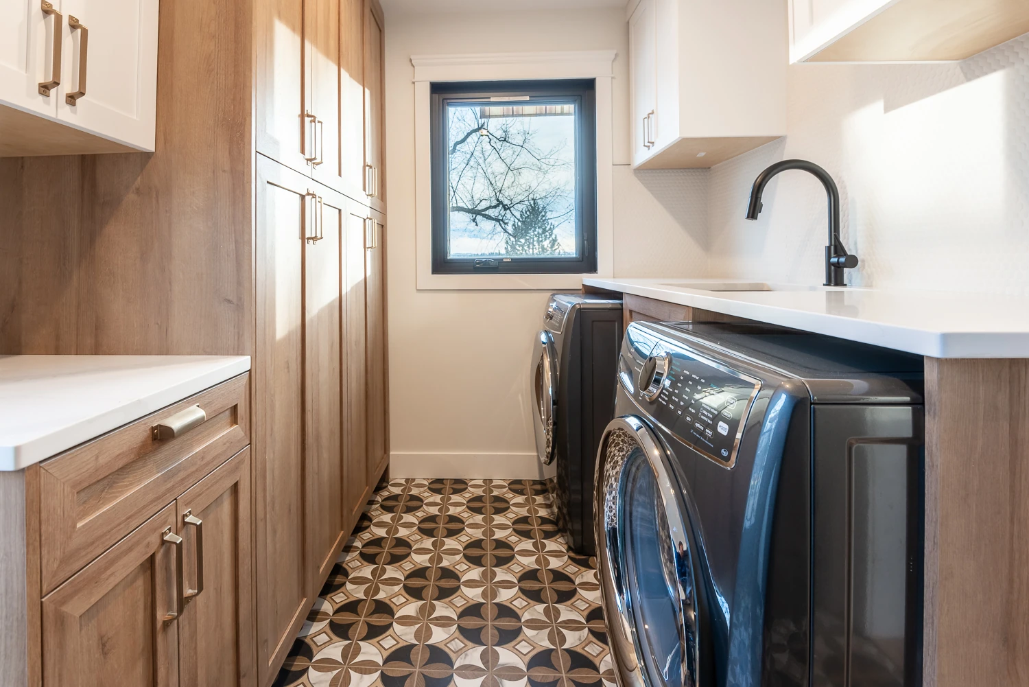 Bright laundry room with warm wood cabinetry, a patterned tile floor, and a large window