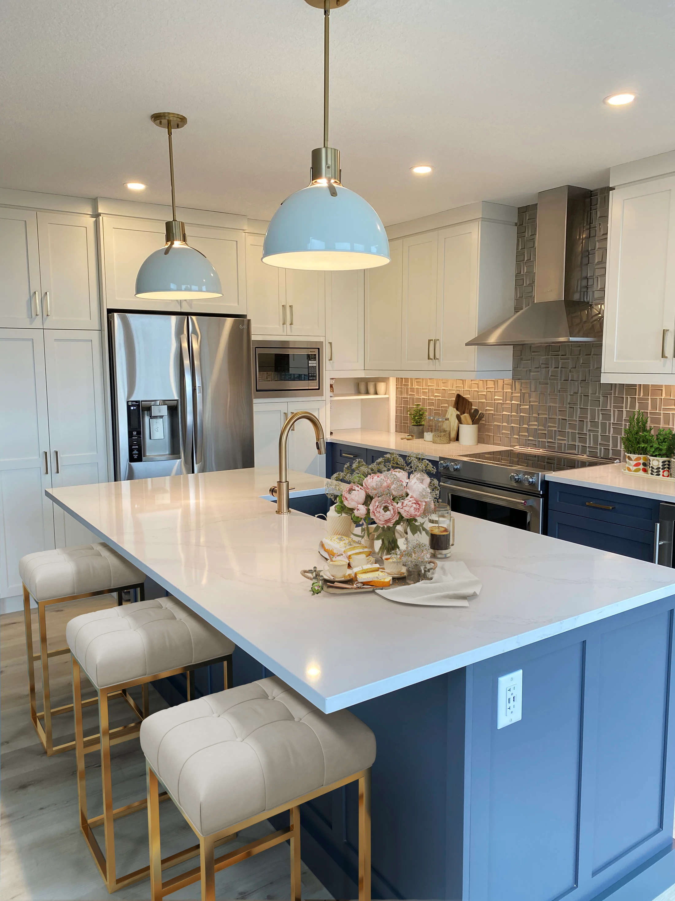 Styled view of a navy and white kitchen with blue pendant lighting and fresh flowers on the island